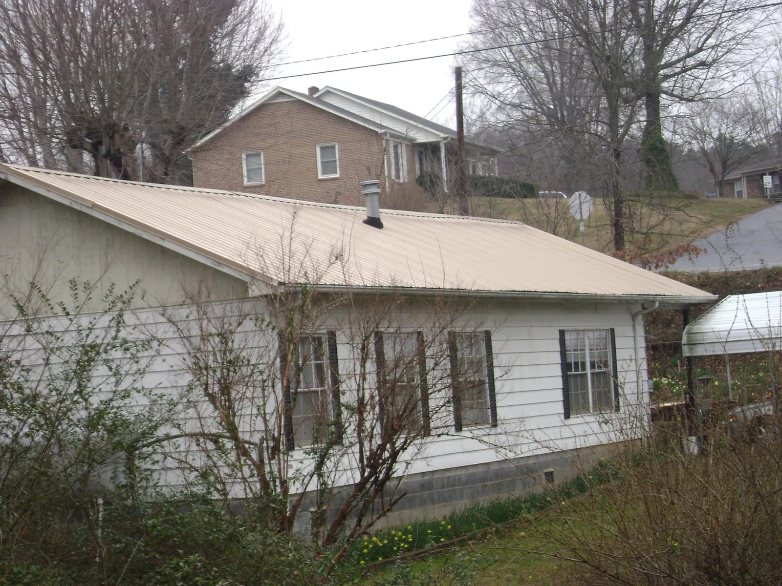 Tan metal roof on a white sided house set into a hillside — Commercial Roofing by Roofing Brothers in Walnut Grove