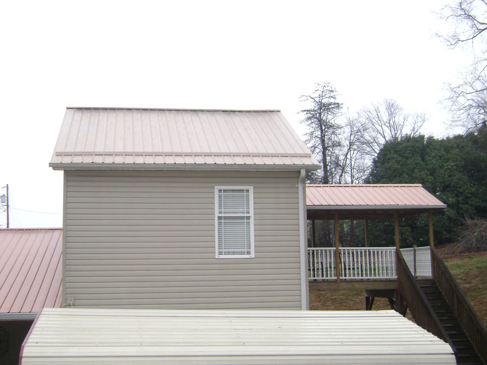 Tan metal roofs on a two story addition and attached porch, from a Roof Replacement job in Walnut Grove